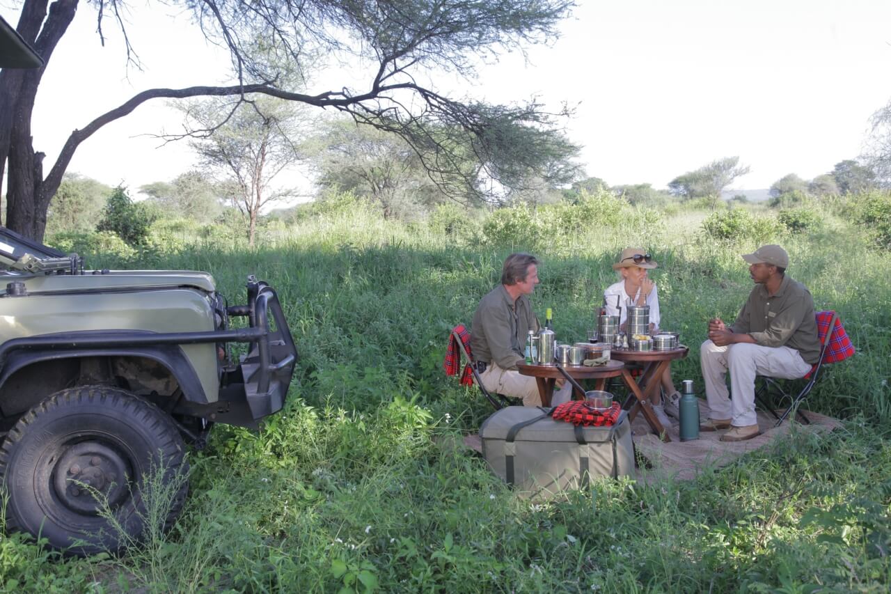 Ein Paar macht während einer Safari mit ihrem Guide eine Pause mit Snacks und Getränken.