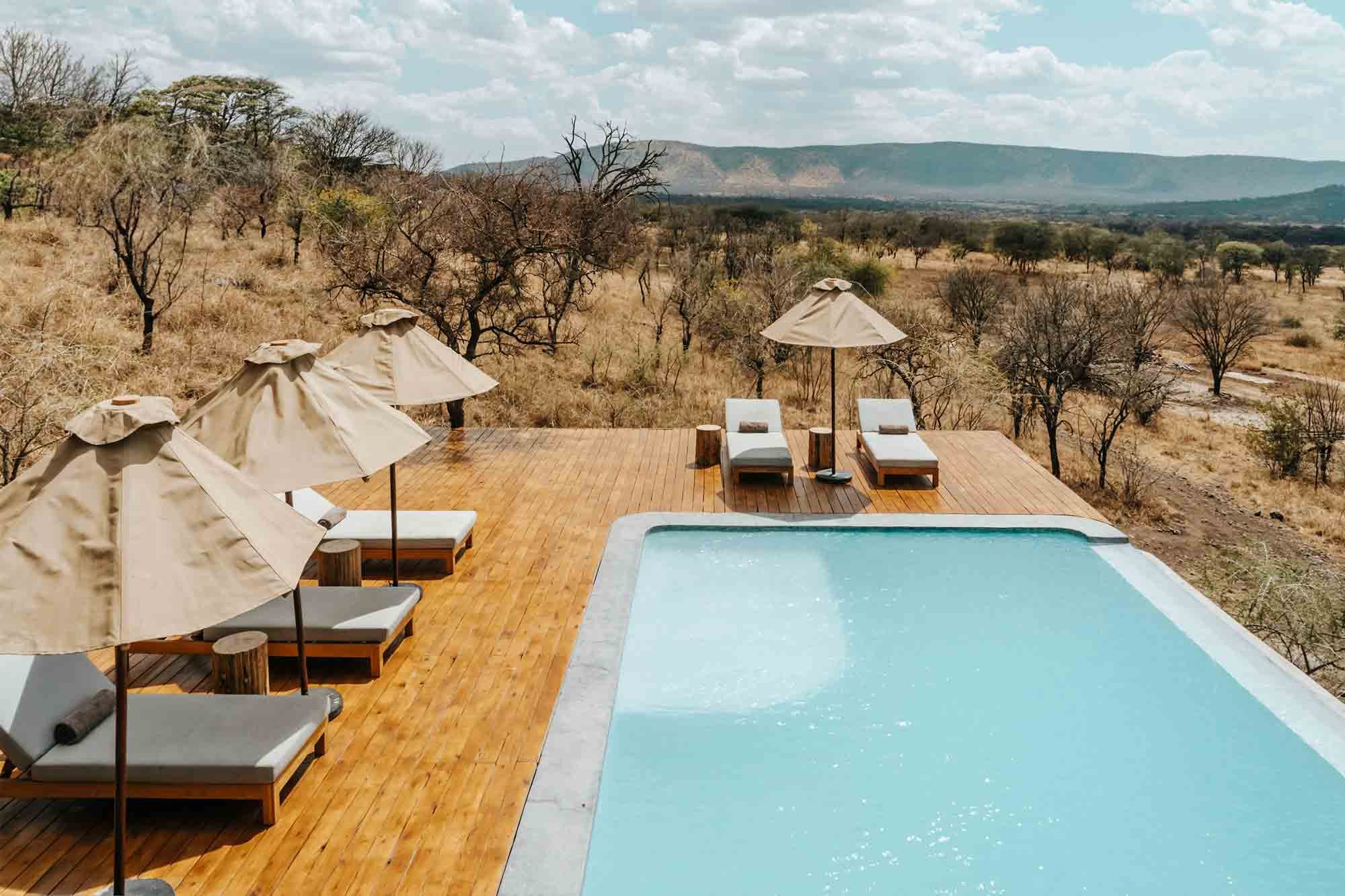 Pool mit Liegen und Sonnenschirmen inmitten der Serengeti.