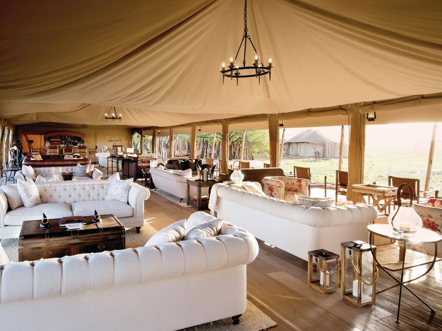 Lounge mit vielen großen, weißen Sofas in einem Safarizelt.