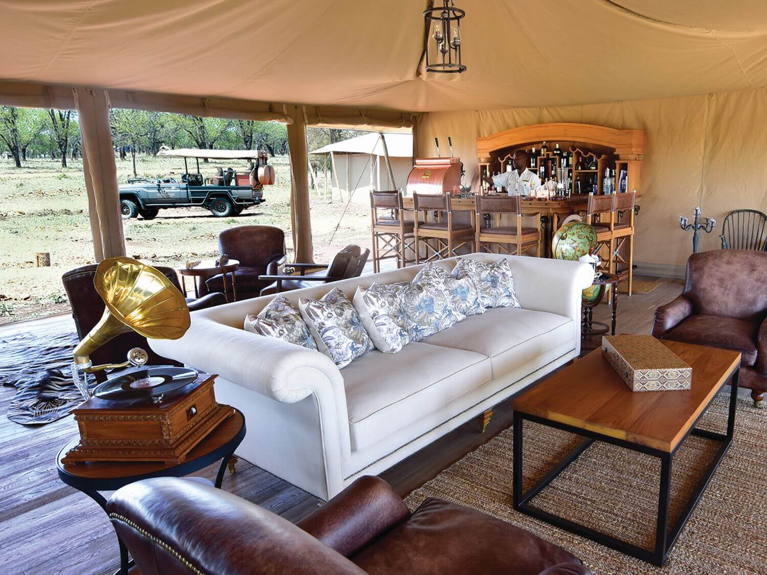 Großes weißes Sofa in einem Safarizelt, draußen fährt ein Safarijeep vor.