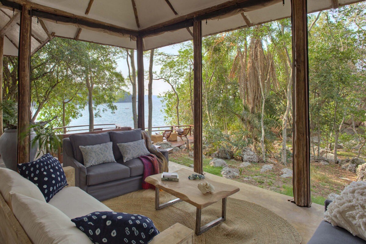 Wohnzimmer einer Lodge mit raumhohen Fenster und Vegetation direkt davor.