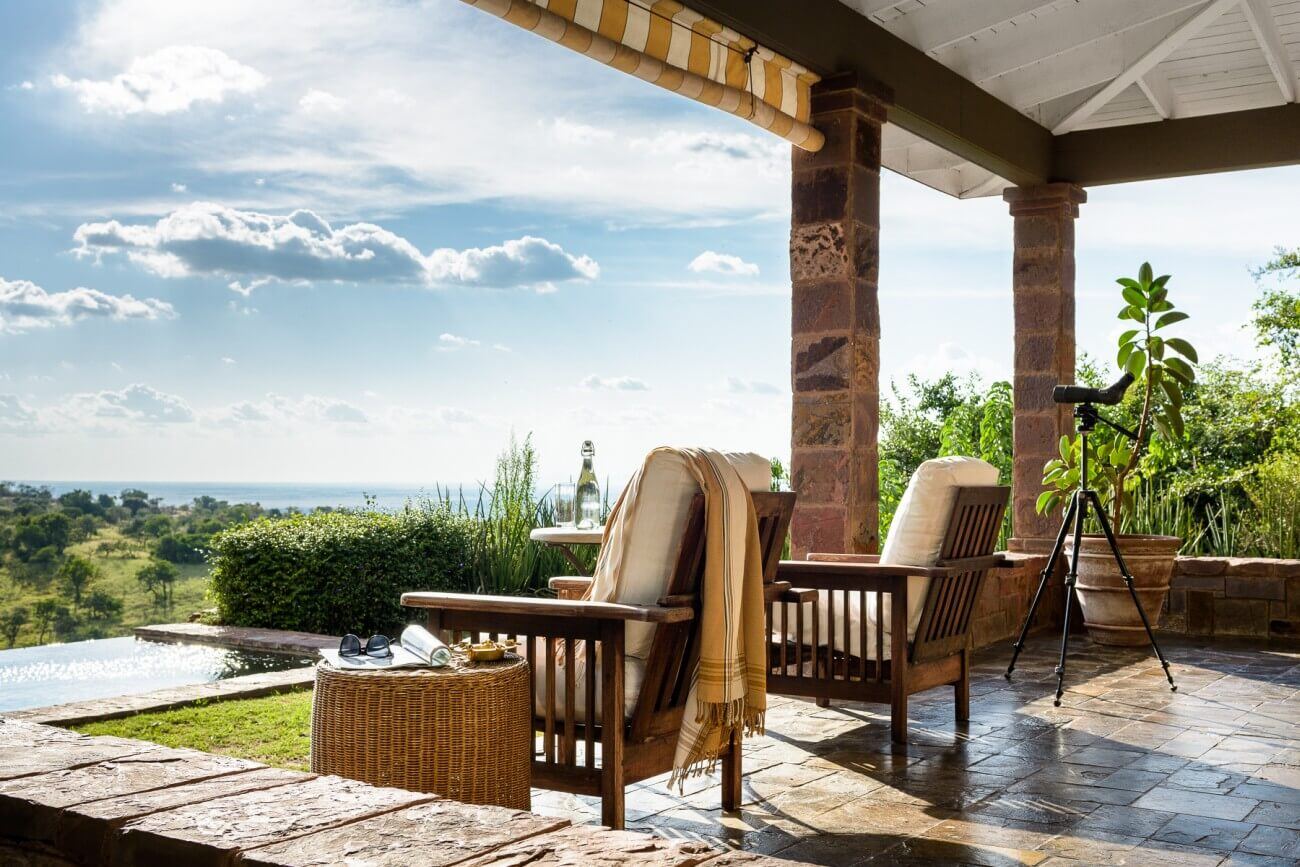 Überdachte Terrasse mit Stühlen und Blick auf Pool und Landschaft.
