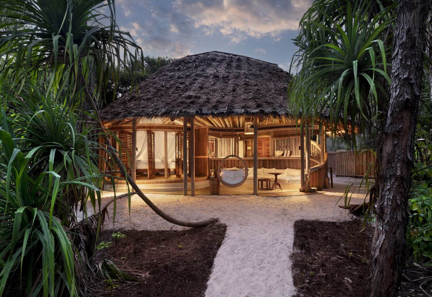 Eine beleuchtete Lodge von außen, ein Sandweg führt auf sie zu.