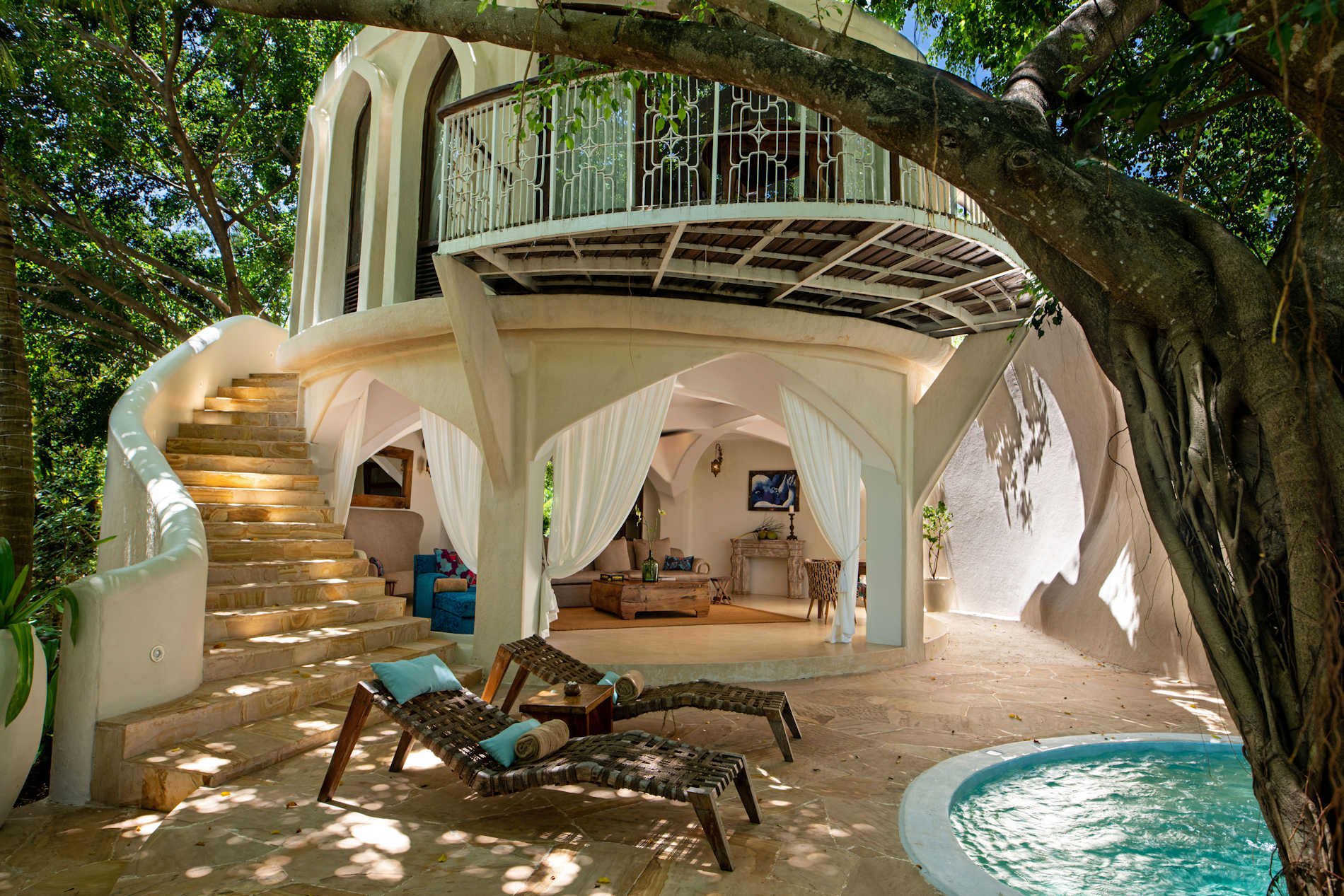 Innenhof einer weißen Luxusvilla mit Außentreppe. Neben dem Pool steht ein Baum.