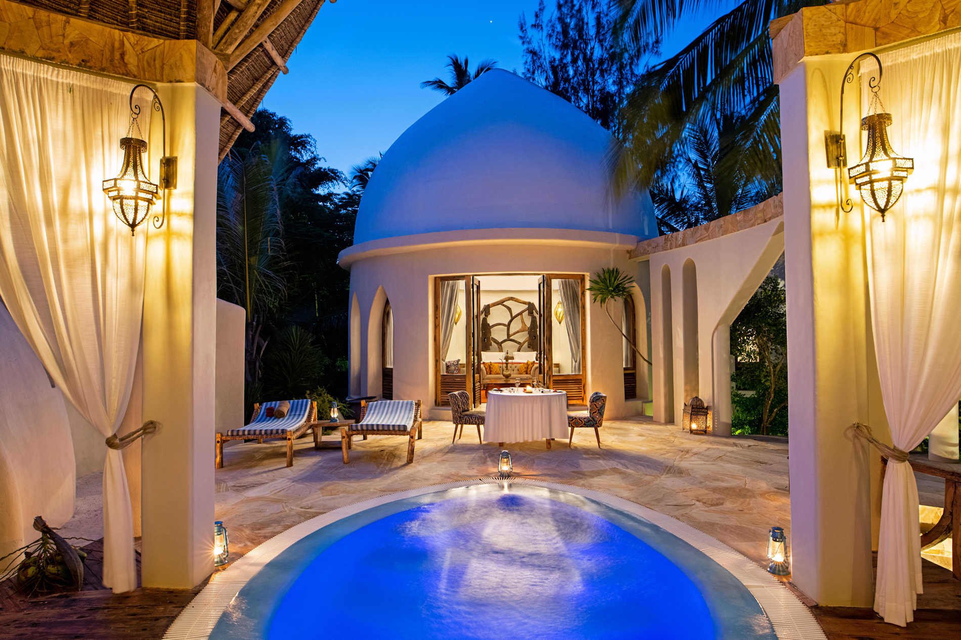 Beleuchtete Villa mit Runddach und einem Pool in der Mitte.