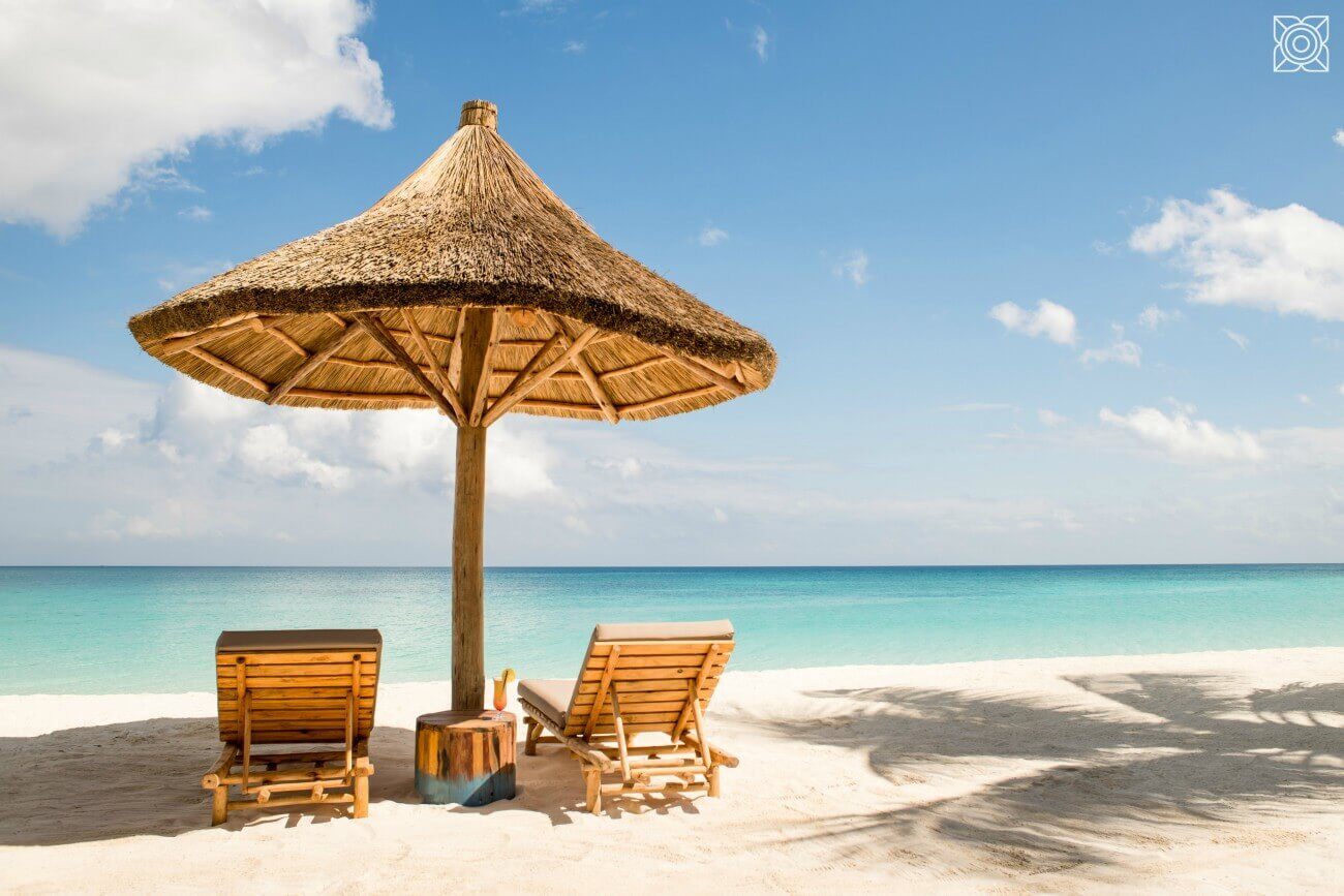 Sonnenschirm aus Reet mit zwei Liegen direkt am Meer.