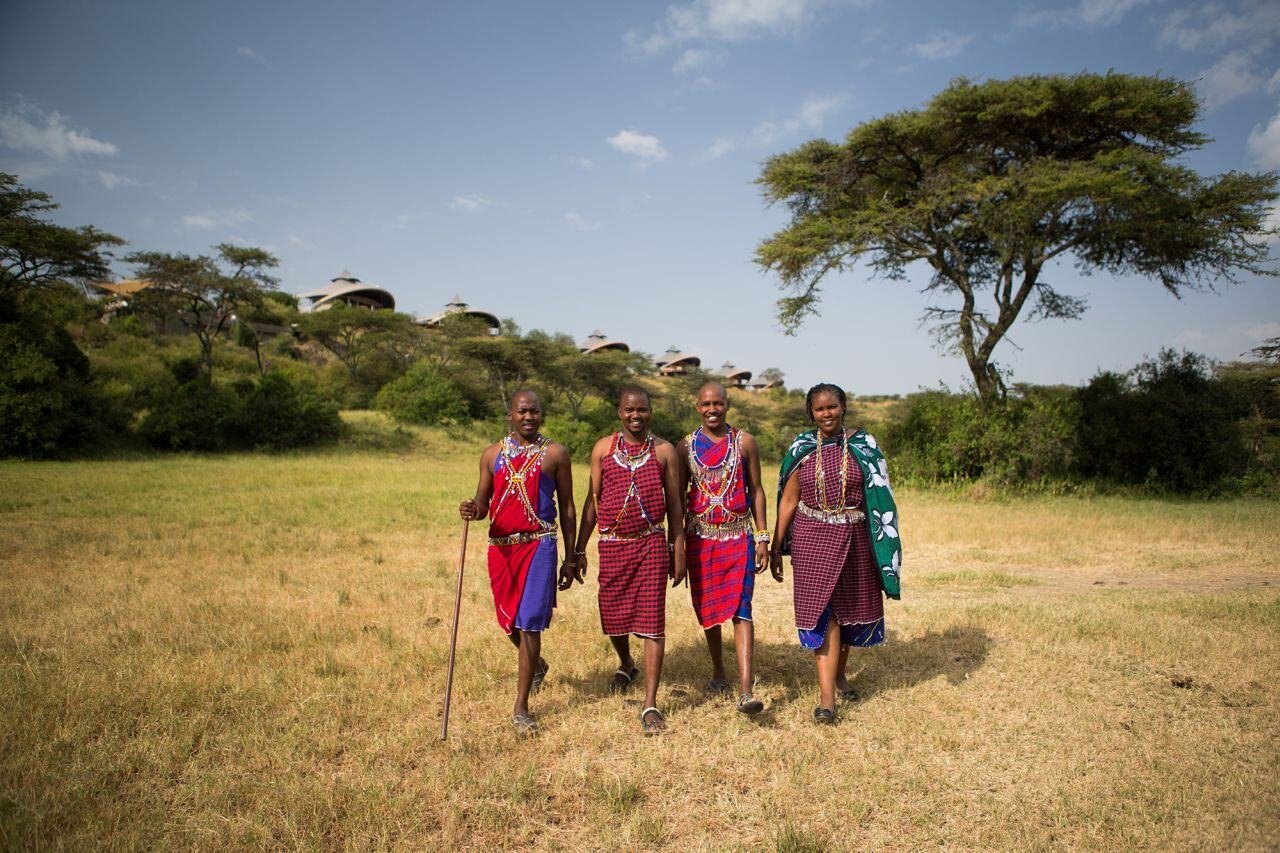 Vier Maasai laufen nebeneinander durch die Savanne.