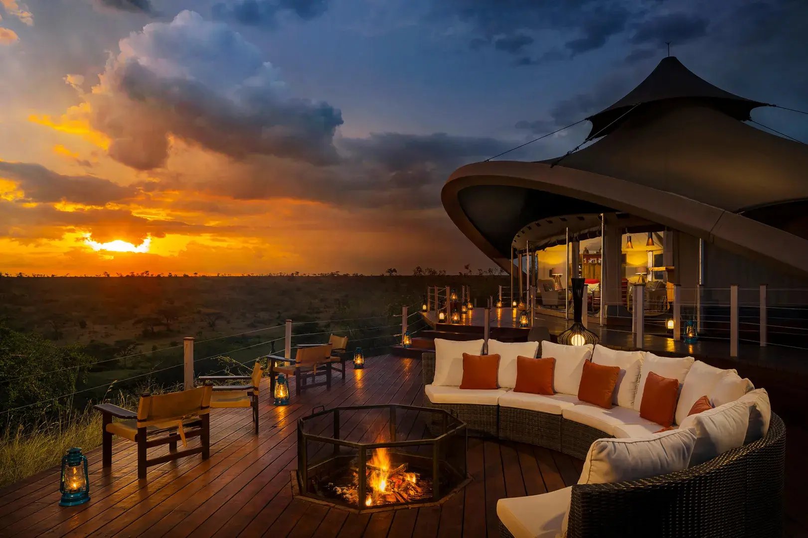 Auf einer Terrasse brennt bei Sonnenuntergang ein Lagerfeuer. Darum ist im Halbkreis eine gemütliche Sitzgelegenheit.