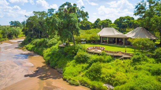 Ein Safaricamp liegt direkt an einem Fluss und ist von üppiger Landschaft umgeben.