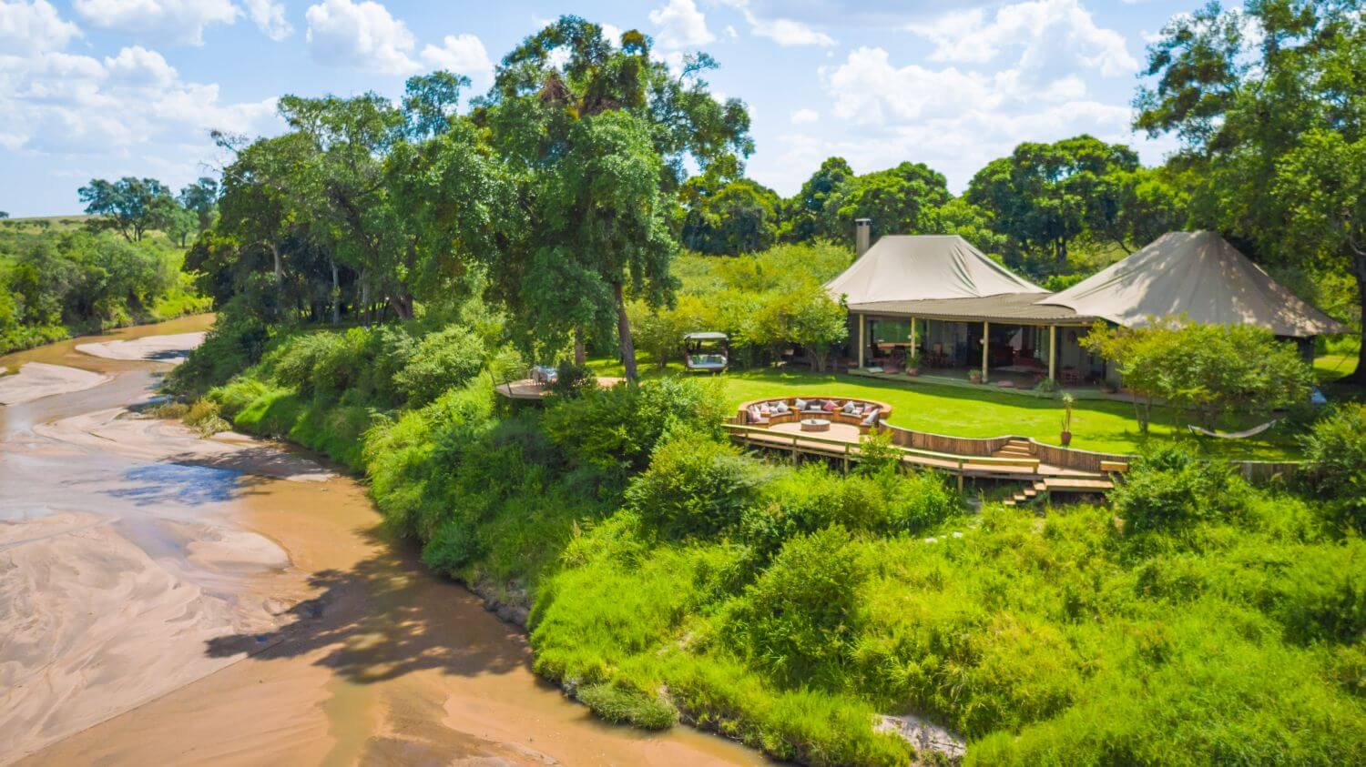 Ein Safaricamp liegt direkt an einem Fluss und ist von üppiger Landschaft umgeben.