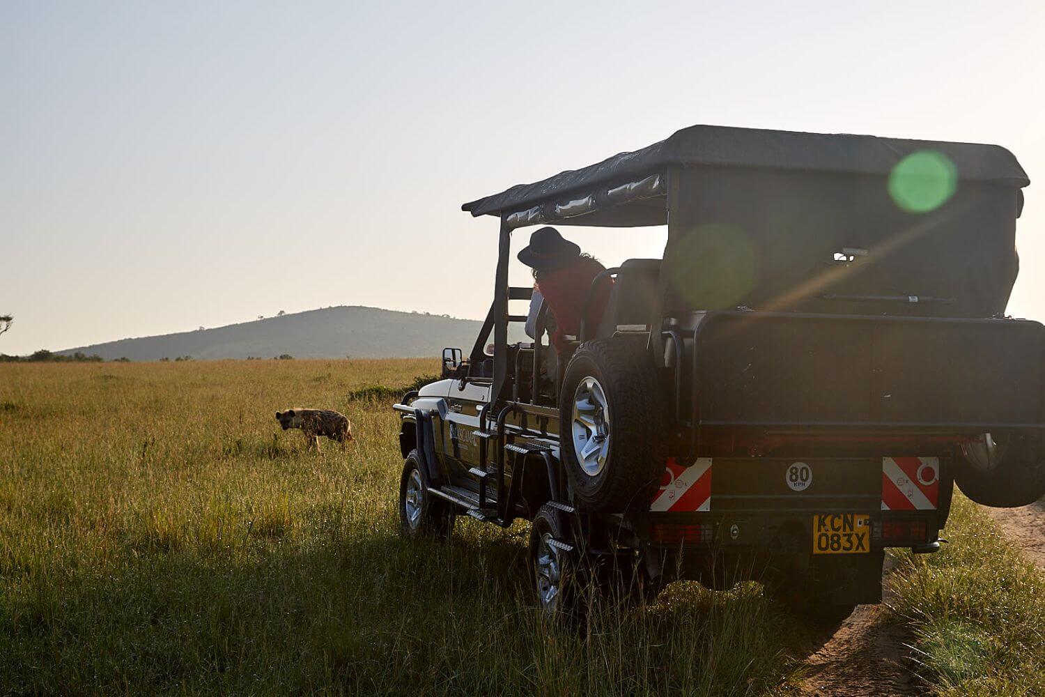 Safarijeep steht vor einer Hyäne.