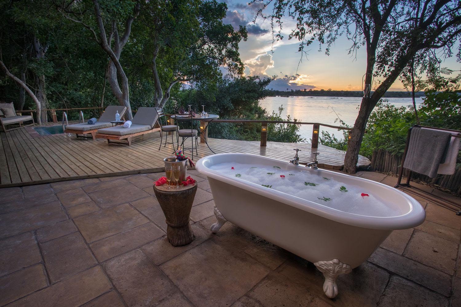 Freistehende Badewanne auf einer Terrasse in natürlicher Umgebung und Fluss im Hintergrund.