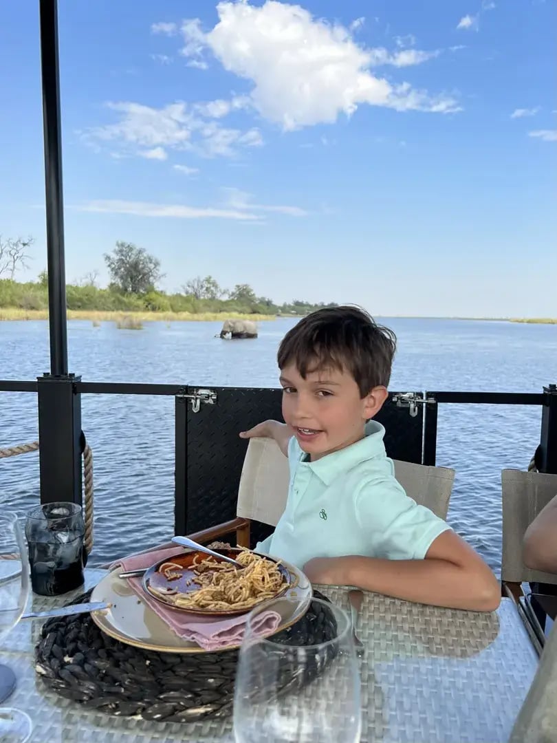 Junge sitzt vor einem Teller mit Essen, im Hintergrund ist ein Fluss zu sehen.