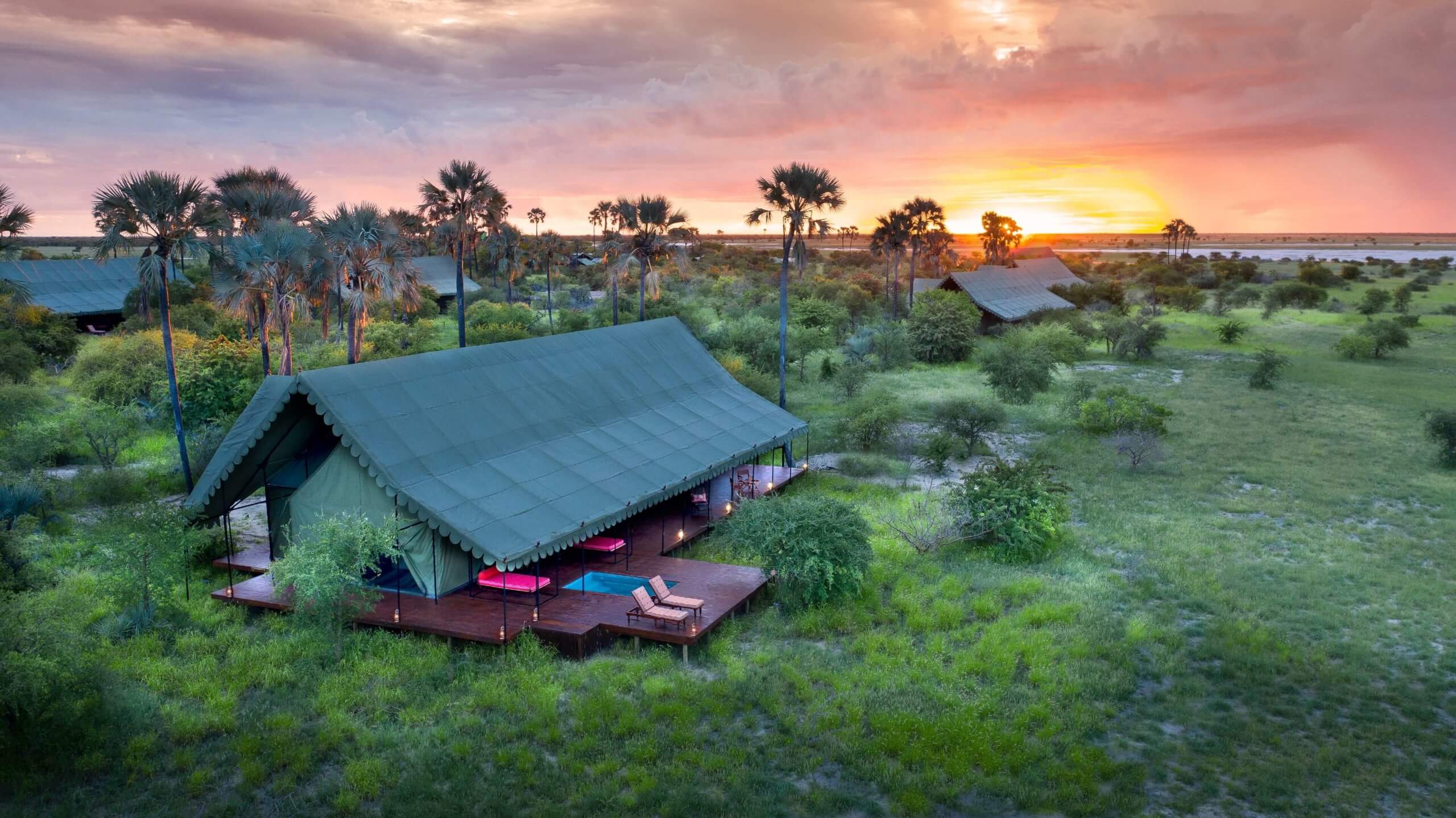 Luftaufnahme eines Zeltes mit Terrasse bei Sonnenuntergang inmitten der Landschaft.