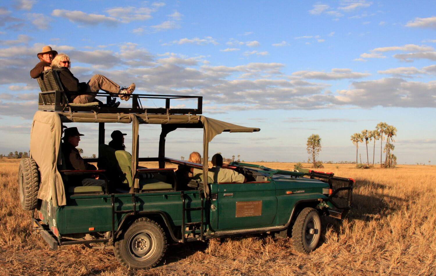 Touristen sind im offenen Jeep auf Safari. Zwei Gäste sitzen auf dem Dach.