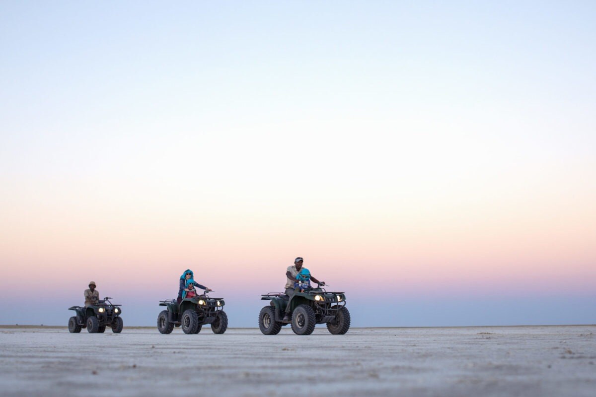 Drei Quads fahren durch die unendliche Weite der Magkadikadi Salzpfannen, Botswana.