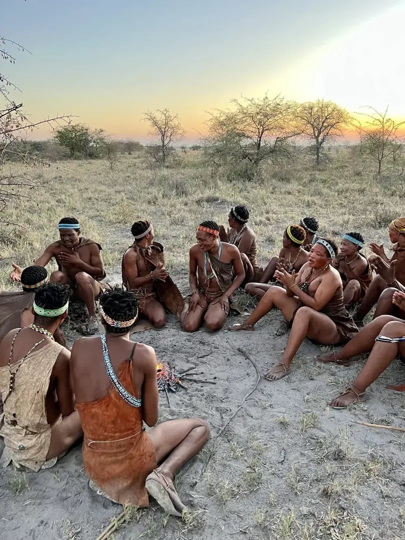 San sitzen im Kreis auf dem Boden in der Makgadikgadi-Salzpfanne, Botswana.