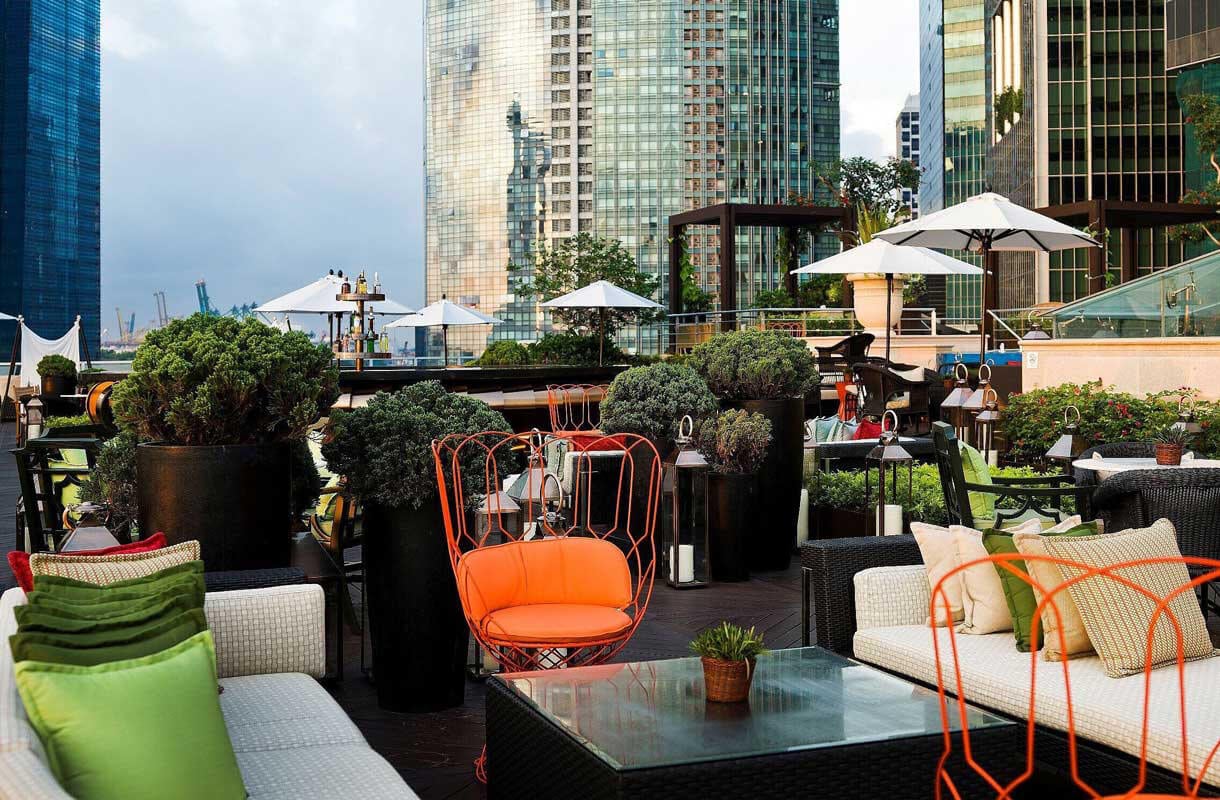 Outdoor Sitzgelegenheiten in der Lantern Seating Area des Fullerton Bay Hotels mit Singapurs Hochhäusern im Hintergrund