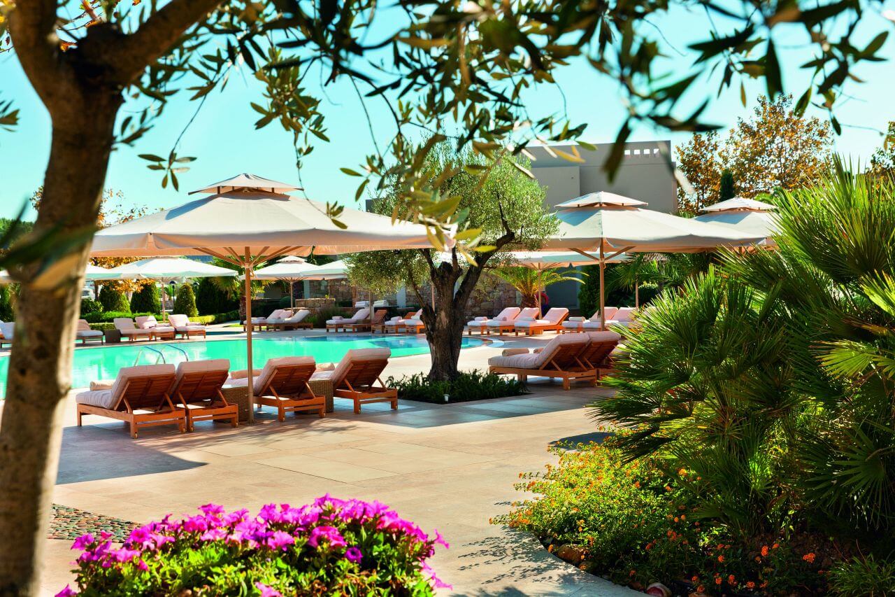 Gartenanlage eines Resorts mit Blumen, Pool und Sonnenbereichen.