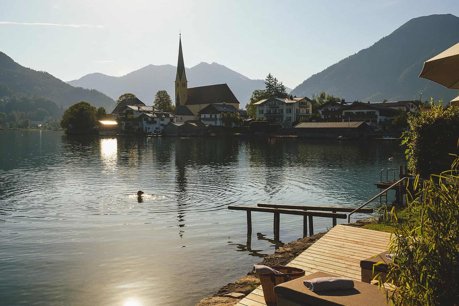 althoff-seehotel-überfahrt terrasse und steg zum see, Dame schwimmt im see bei Sonnenschein