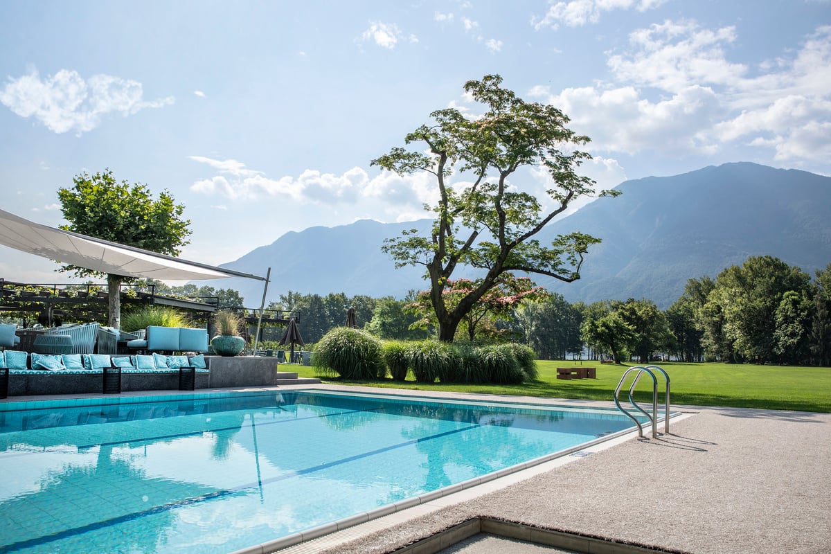 Swimmingpool in einem großen Garten, im Hintergrund thronen Berge.