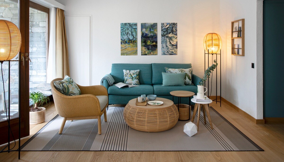 Wohnzimmer mit türkisem Sofa und Korbmöbeln.