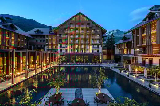 Beleuchtete Hotelanlage in der Dämmerung, im Zentrum ist ein Pool.
