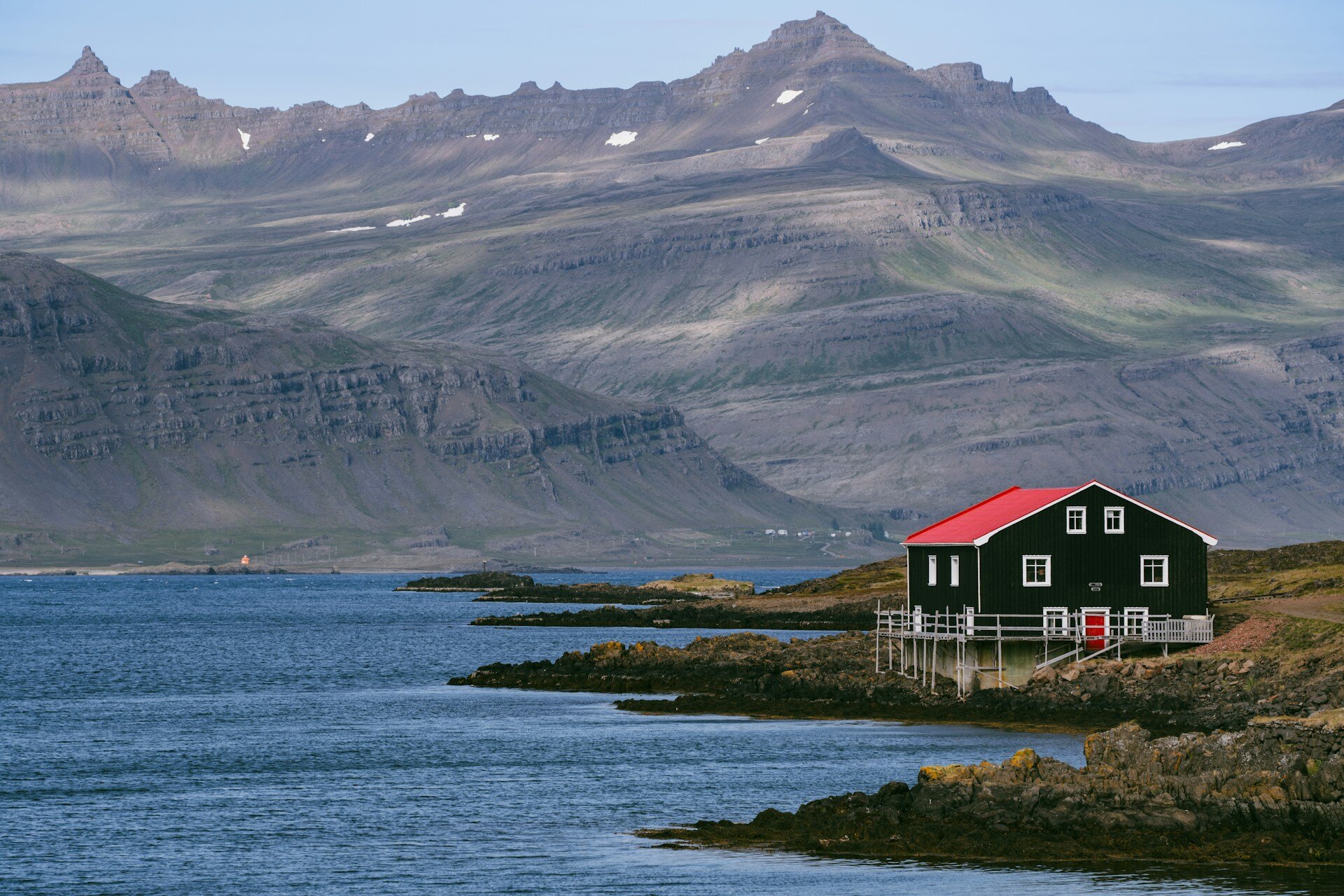 ein Haus mit rotem Dach am Meer gelegen mit Bergen im Hintergrund