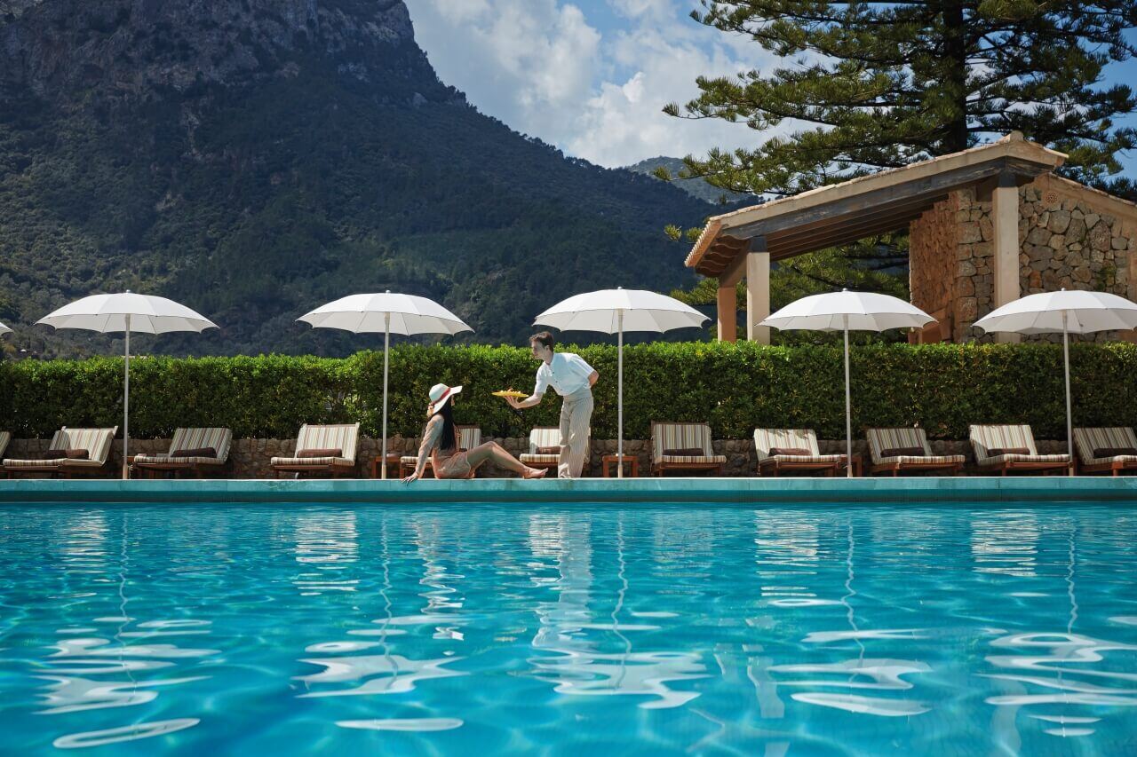 Ein Kellner serviert einer Frau am Pool Getränke.