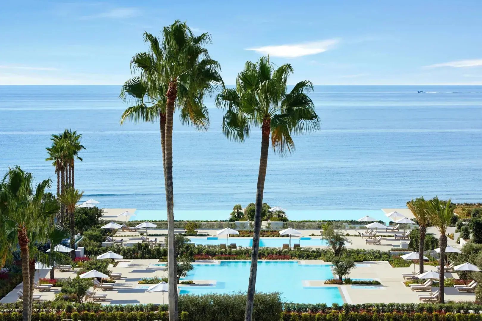 Blick von einer Hotelanlage über einen Pool mit Palmen aufs Meer.