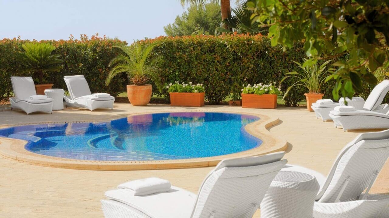 Kleiner Pool mit weißen Sonnenliegen.