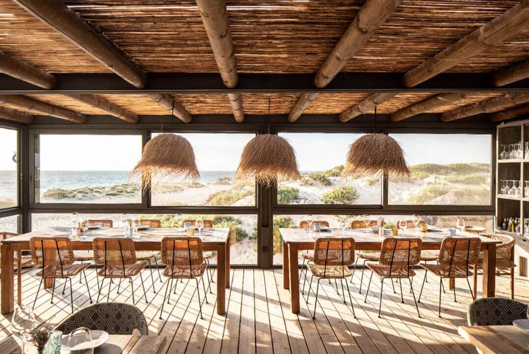 Überdachte Terrasse aus Naturmaterialien mit Stühlen, die Richtung Strand blicken.