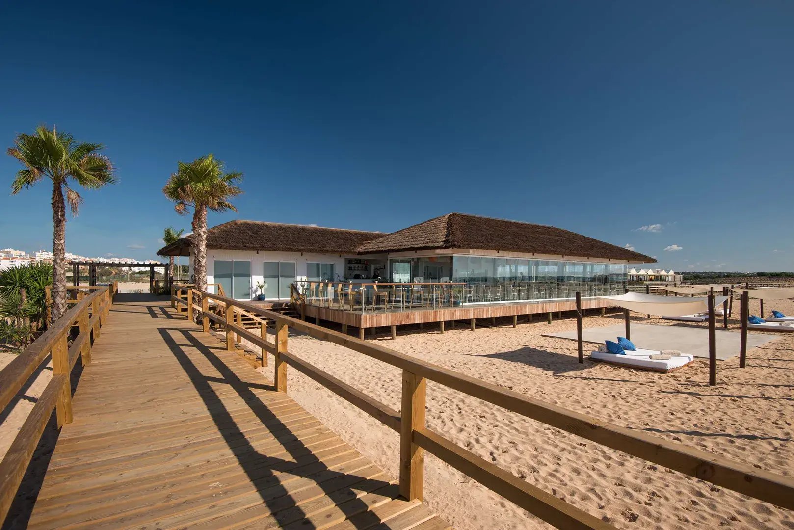 Strandabschnitt mit Holzpfad, der zu einem Restaurant führt.