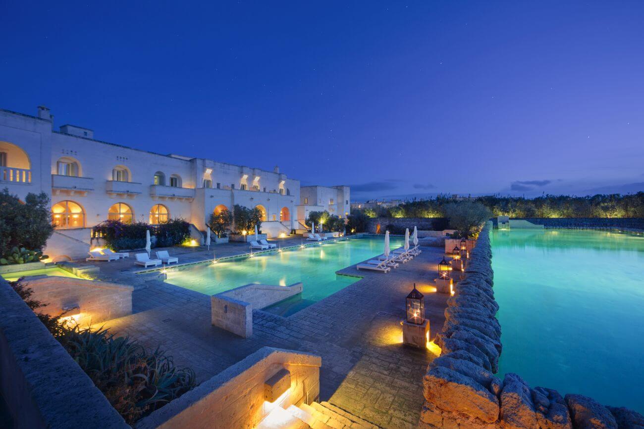 Beleuchteter Pool am Abend mit Anwesen im Hintergrund.