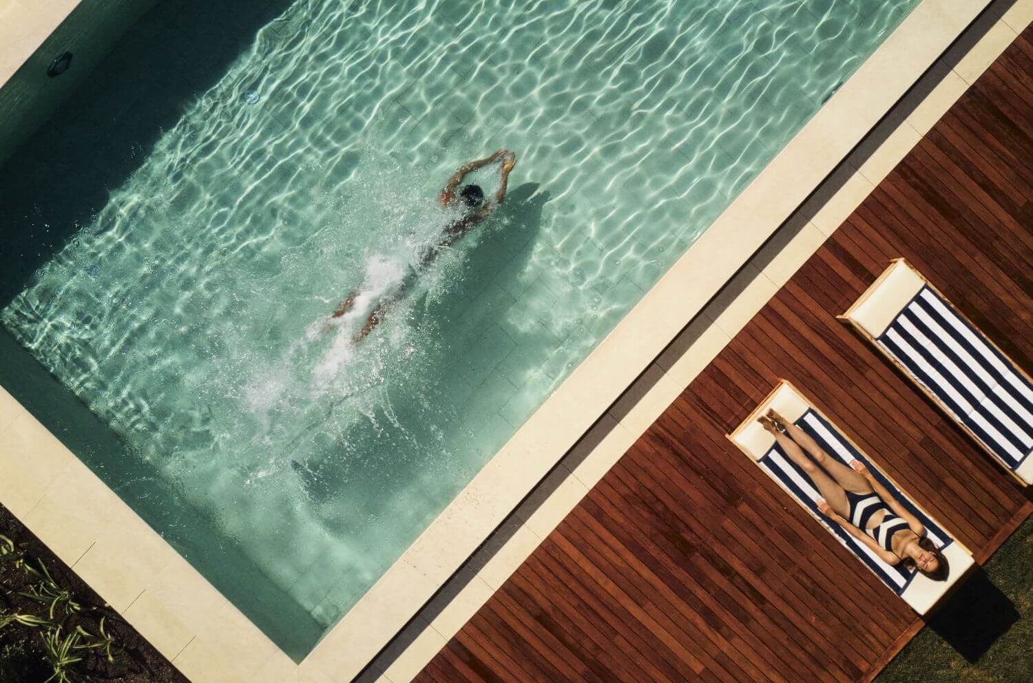 Eine Frau zieht Bahnen in einem Pool, während sich eine andere auf einer Liege sonnt.