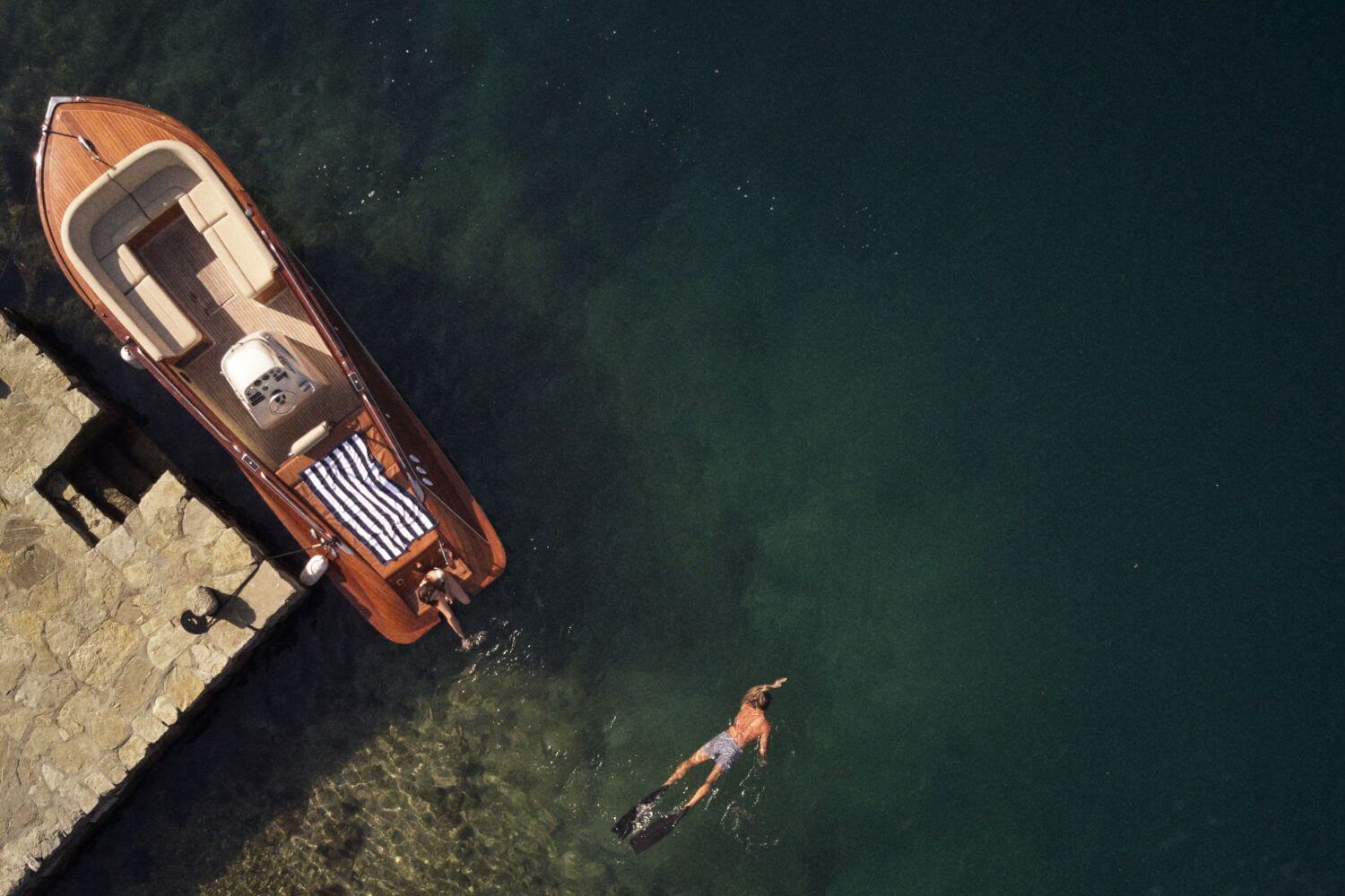 Mann schwimmt im See am Steg neben einem Boot.