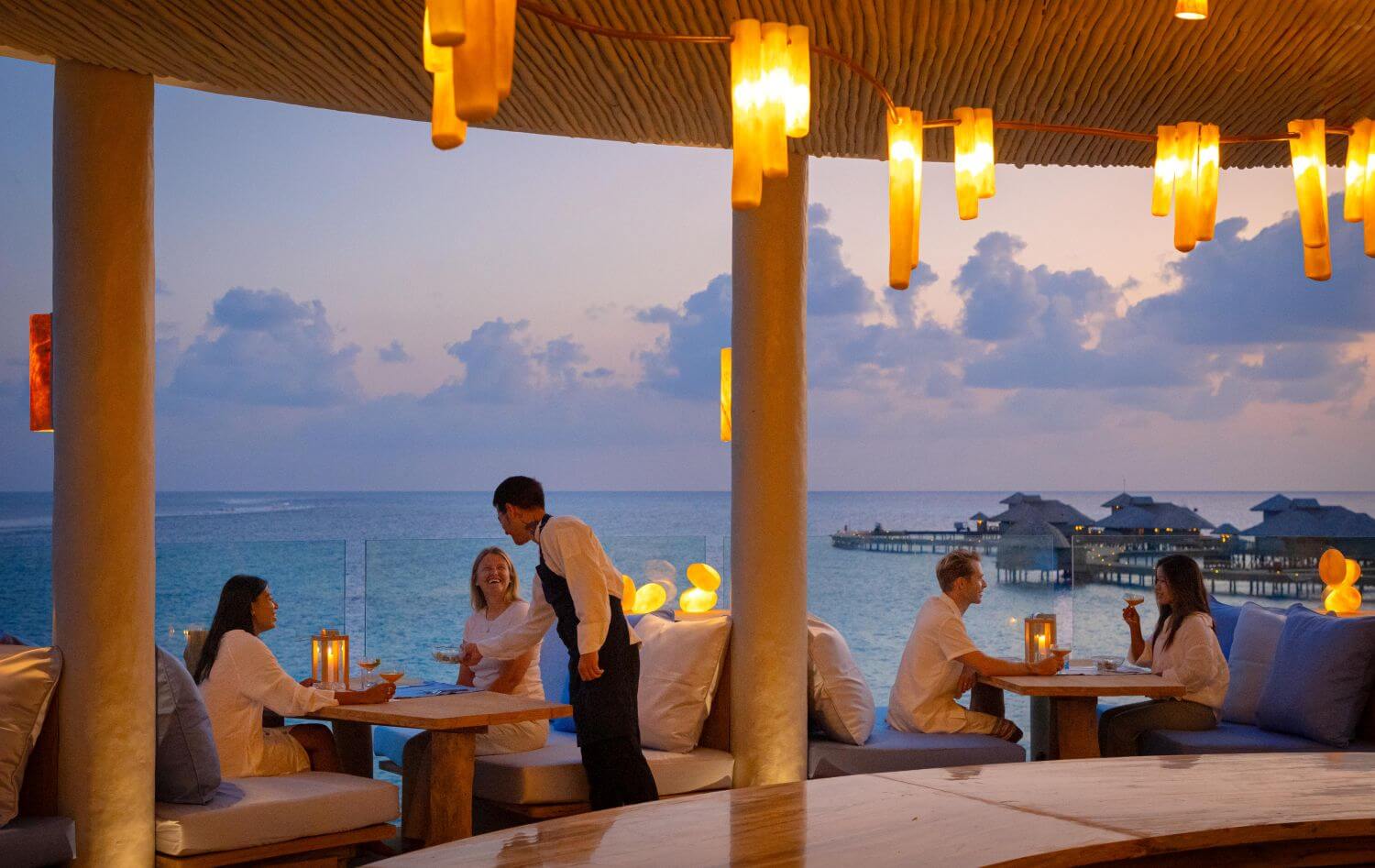 Gäste in einem Restaurant mit Meerblick bei abendlicher Stimmung