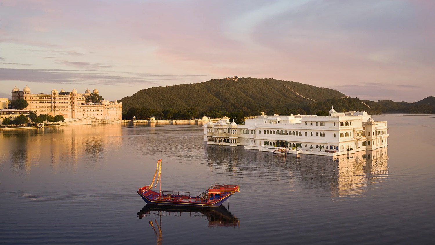 Hotel auf einem See mit grünem Hügel im Hintergrund.