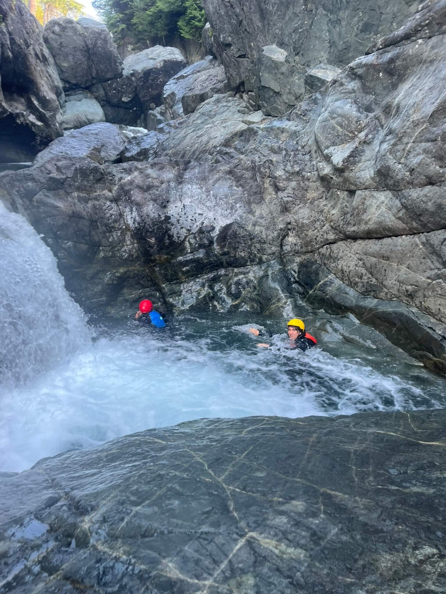 Zwei Personen schwimmen beim Canyoning an einem kleinen Wasserfall vorbei.