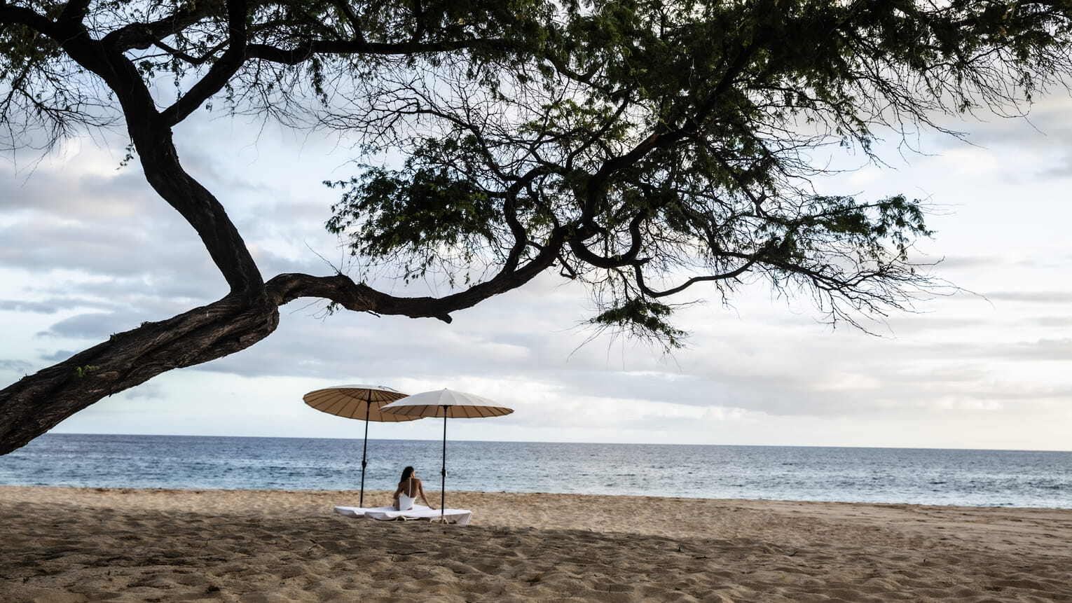 four seasons resort lanai Frau sitzt unter zwei Sonnenschirmen am leeren Strand