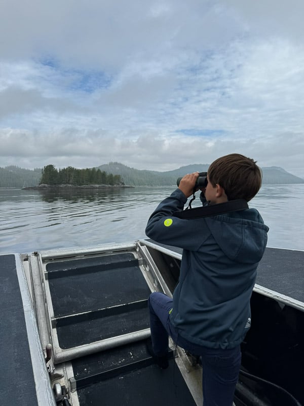 Ein Junge sucht auf einem Boot mit einem Fernglas die Küste nach Tieren ab.
