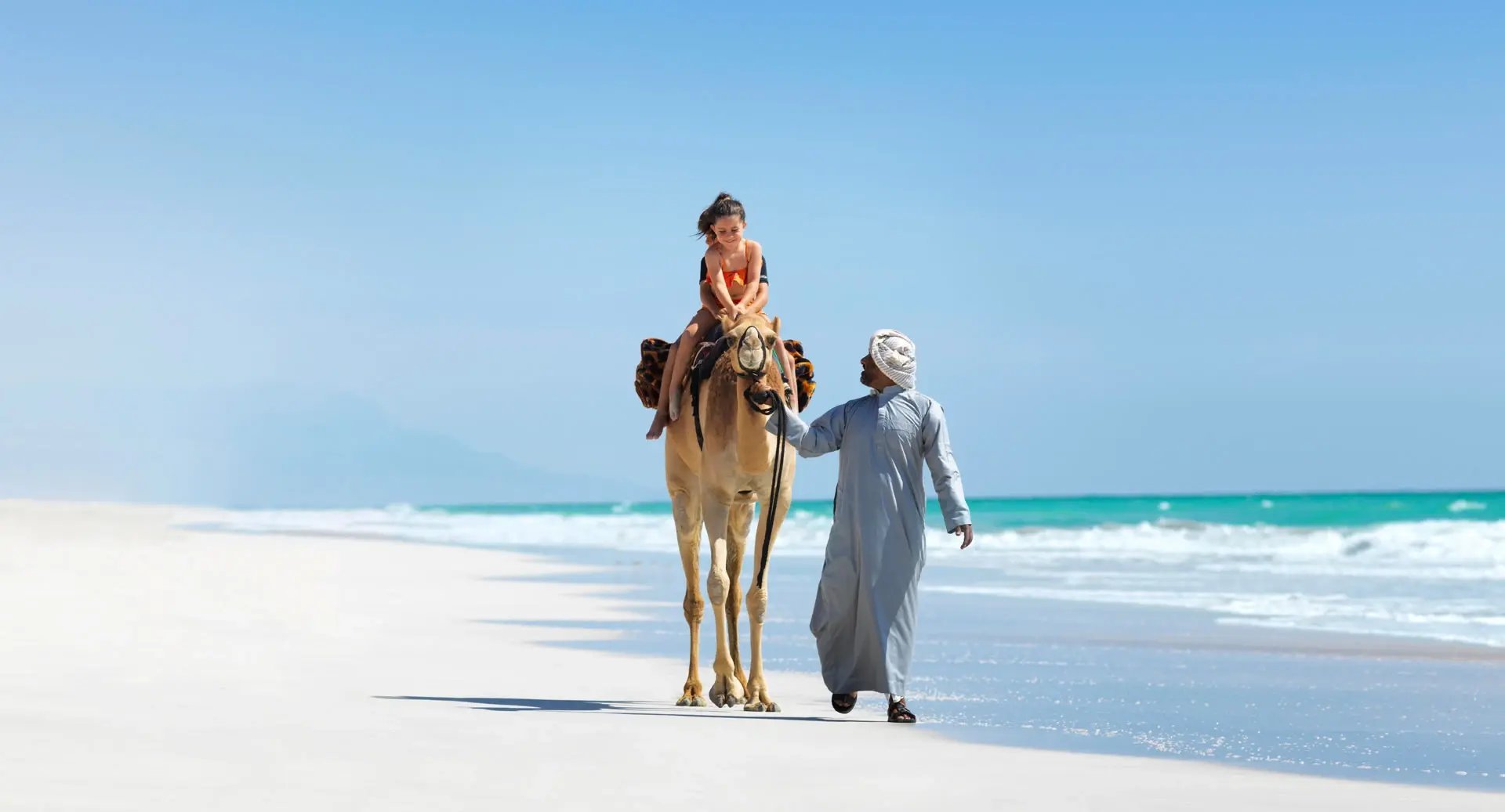 Ein Kind reitet auf einem Kamel am Strand entlang.