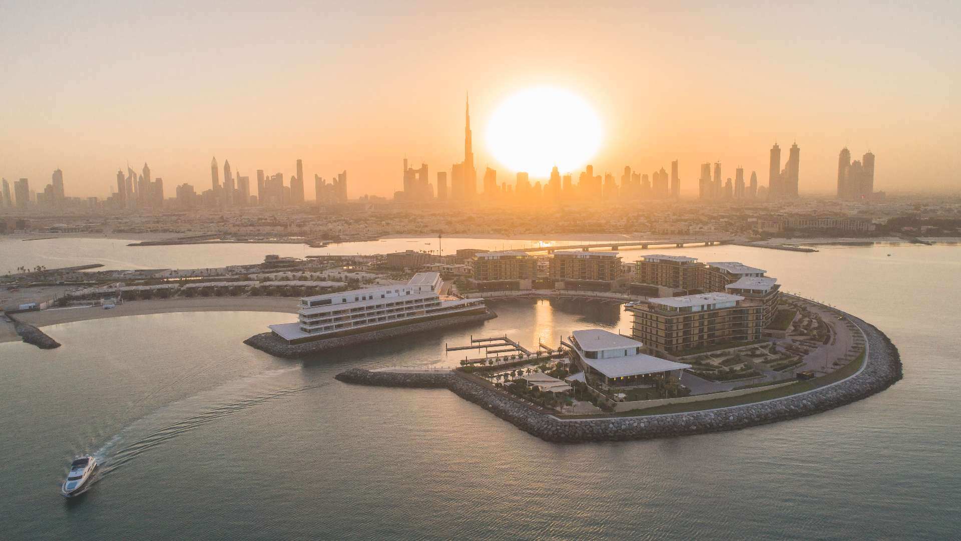 Insel mit Luxusresort bei tiefstehender Sonne. Die Skyline Dubais im Hintergrund.