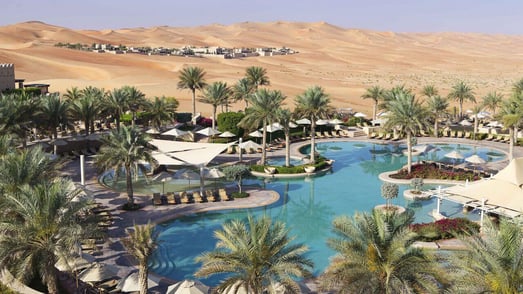 Poolandschaft mit Palmen eines Resorts in der Wüste.