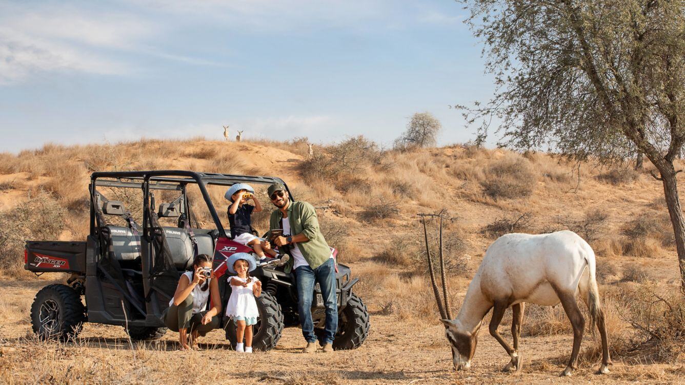 Eine Familie steht in der Wildnis vor einer weißen Oryxantilope.