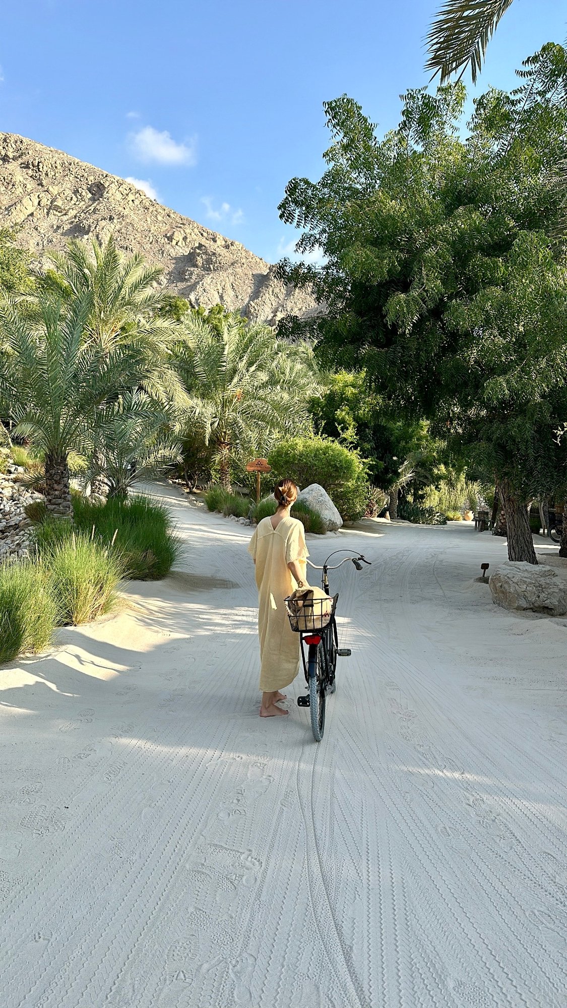Eine Frau schiebt ein Fahrrad über die Anlage von Zighy Bay