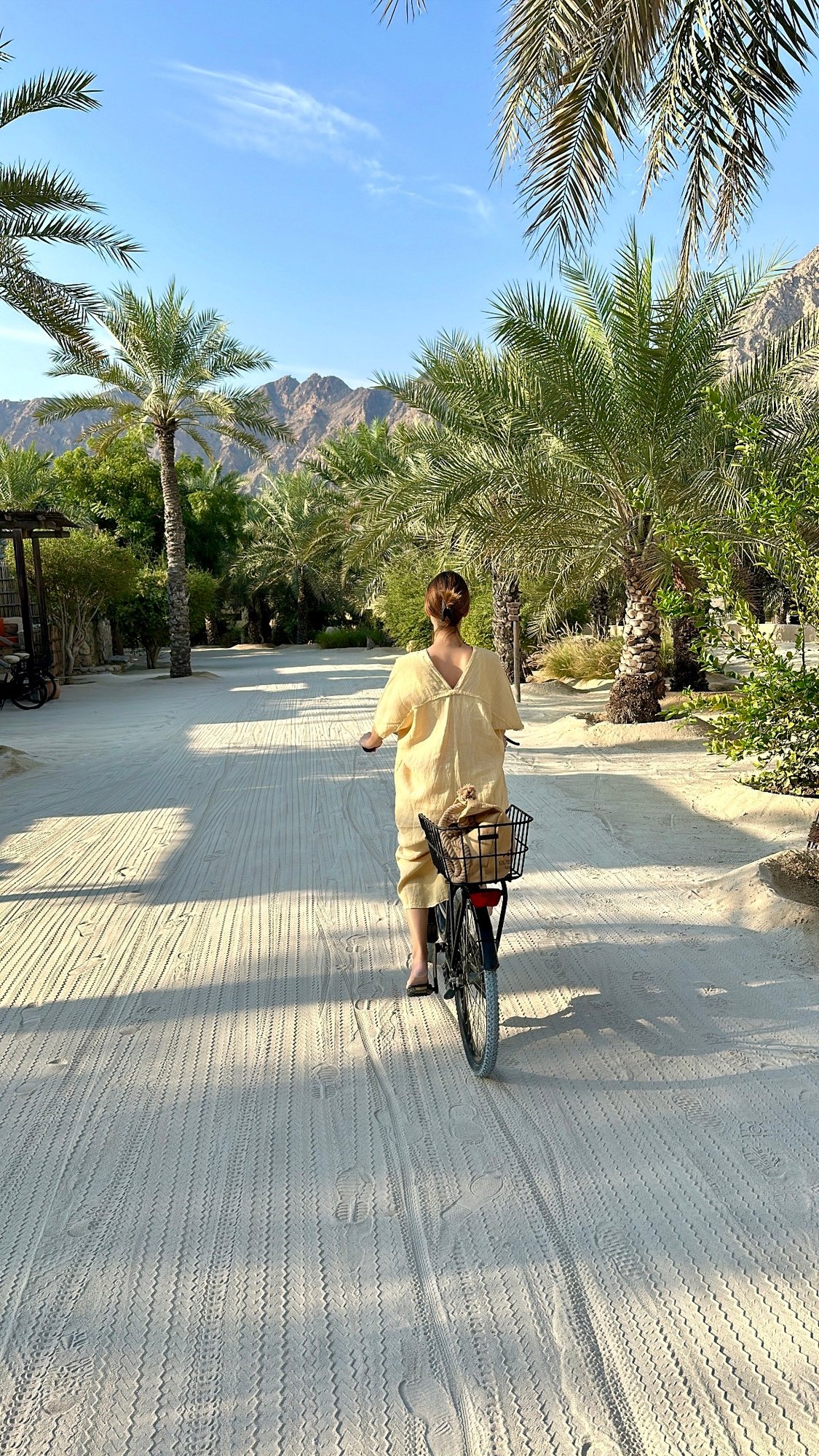 Frau radelt zwischen Palmen im Resort Zighy Bay, Oman