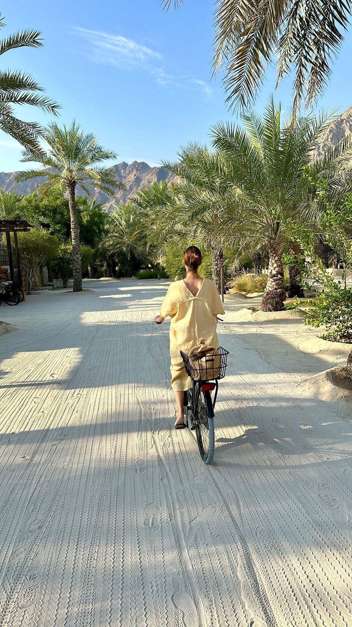 Frau radelt zwischen Palmen im Resort Zighy Bay, Oman