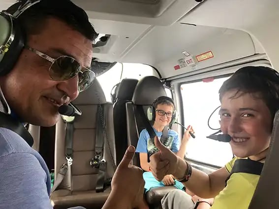 Ein Vater mit zwei Söhnen sitzen angeschnallt in einem Privatjet und zeigen lachend die Daumen-hoch-Geste in die Kamera