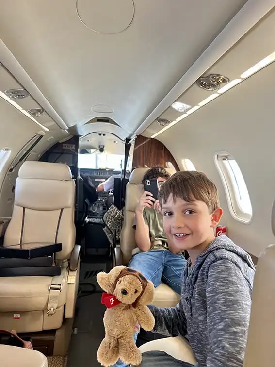 Zwei Jungs mit Handy und Stofftier in der Hand fliegen in einem Privatjet zu ihrem Urlaubsziel